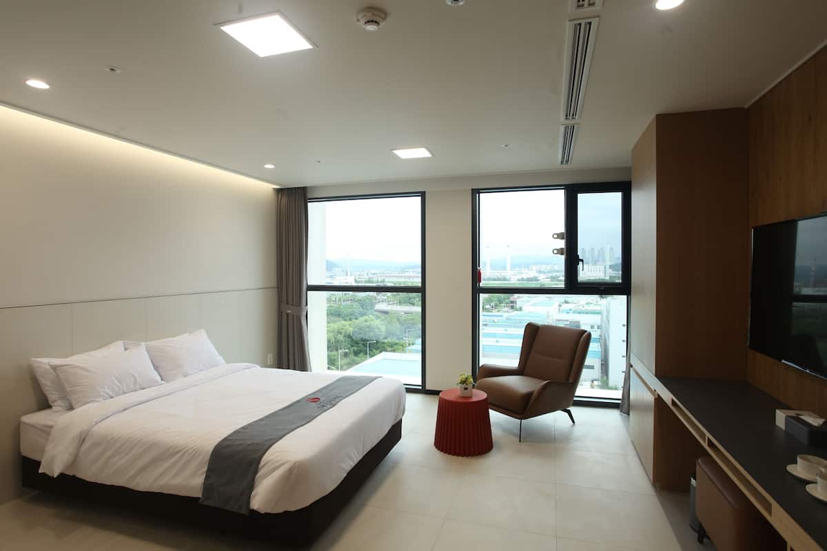 Een moderne hotelkamer met een groot bed, een bureau met een flatscreen televisie, een stoel en een bijzettafeltje met een plant.