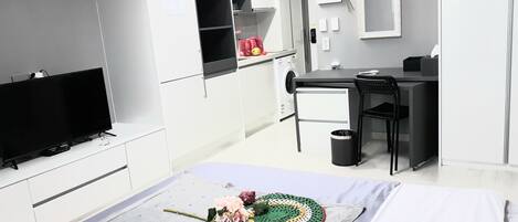 A modern hotel room with a flat-screen TV, a desk, a chair, a small trash bin, and a decorative crocheted item on the bed.