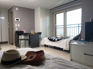 A hotel room with a bed, a desk, a chair, a TV, and a balcony with a view. - Ara Palace Hotel (Jeju City)
