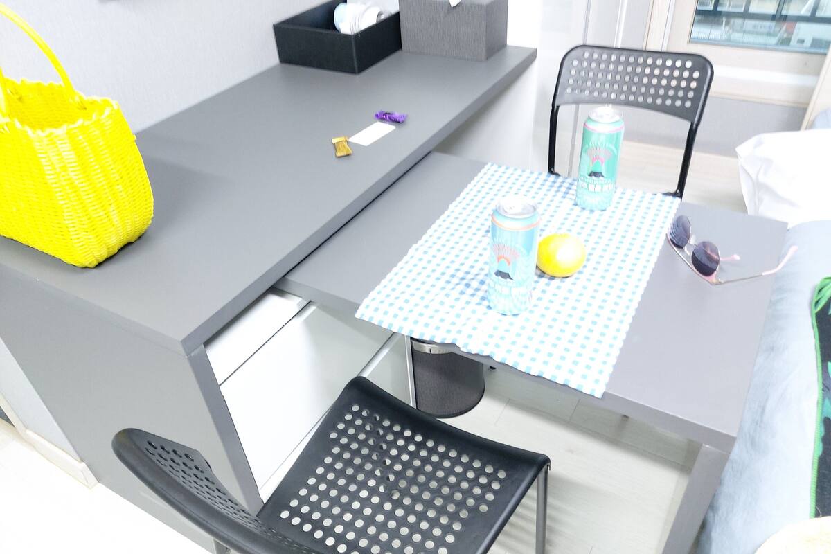 A modern room with a grey table, two black chairs, a yellow basket, a tissue box, a can, and a pair of sunglasses on the table.