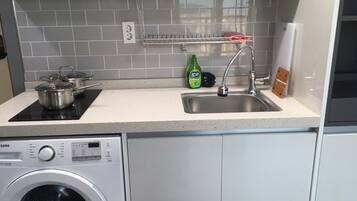 A compact kitchen with a built-in washing machine, a sink, and a dish rack.