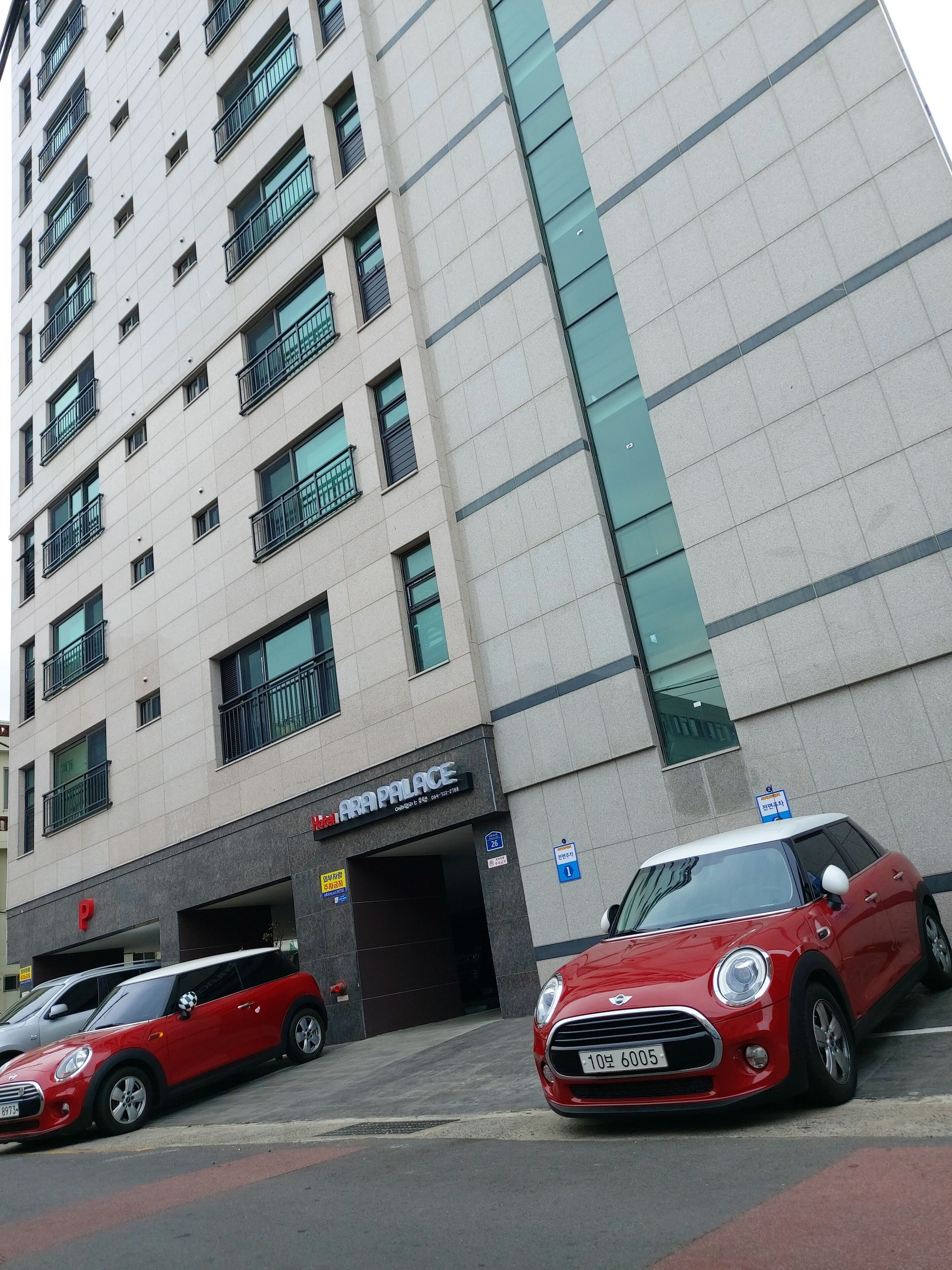 Un edificio de varios pisos con un cartel que dice 'ARA PALACE' en la entrada. Hay dos coches estacionados adelante, uno rojo y uno plateado.