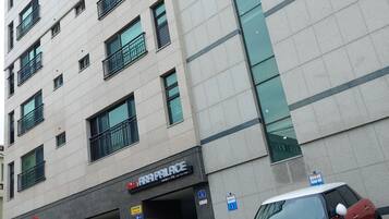 Un edificio de varios pisos con un cartel que dice 'ARA PALACE' en la entrada. Hay dos coches estacionados adelante, uno rojo y uno plateado.