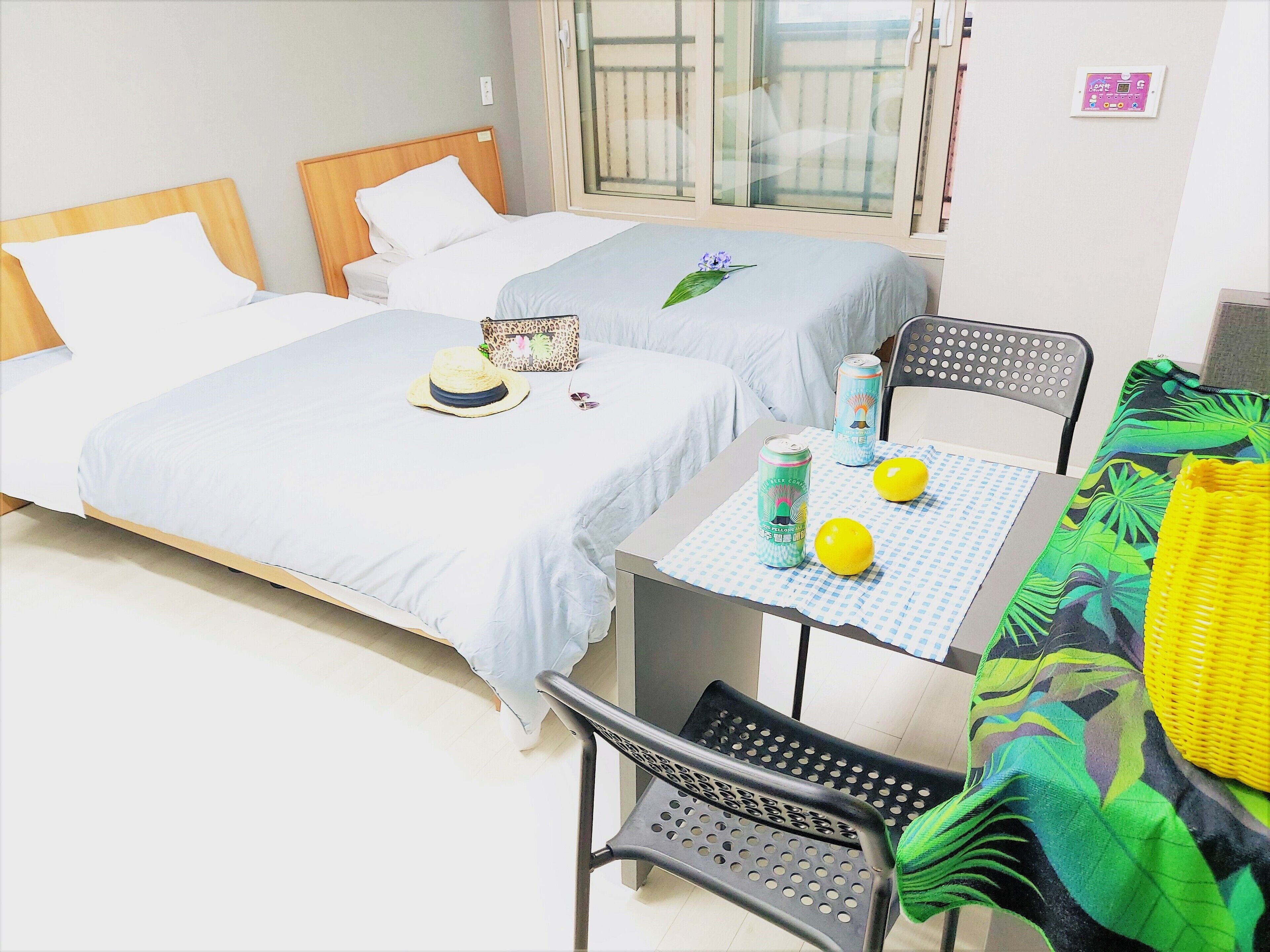 Une chambre d’hôtel avec deux lits, une table sur laquelle se trouvent deux canettes et deux citrons, une chaise et une fenêtre donnant sur un balcon.