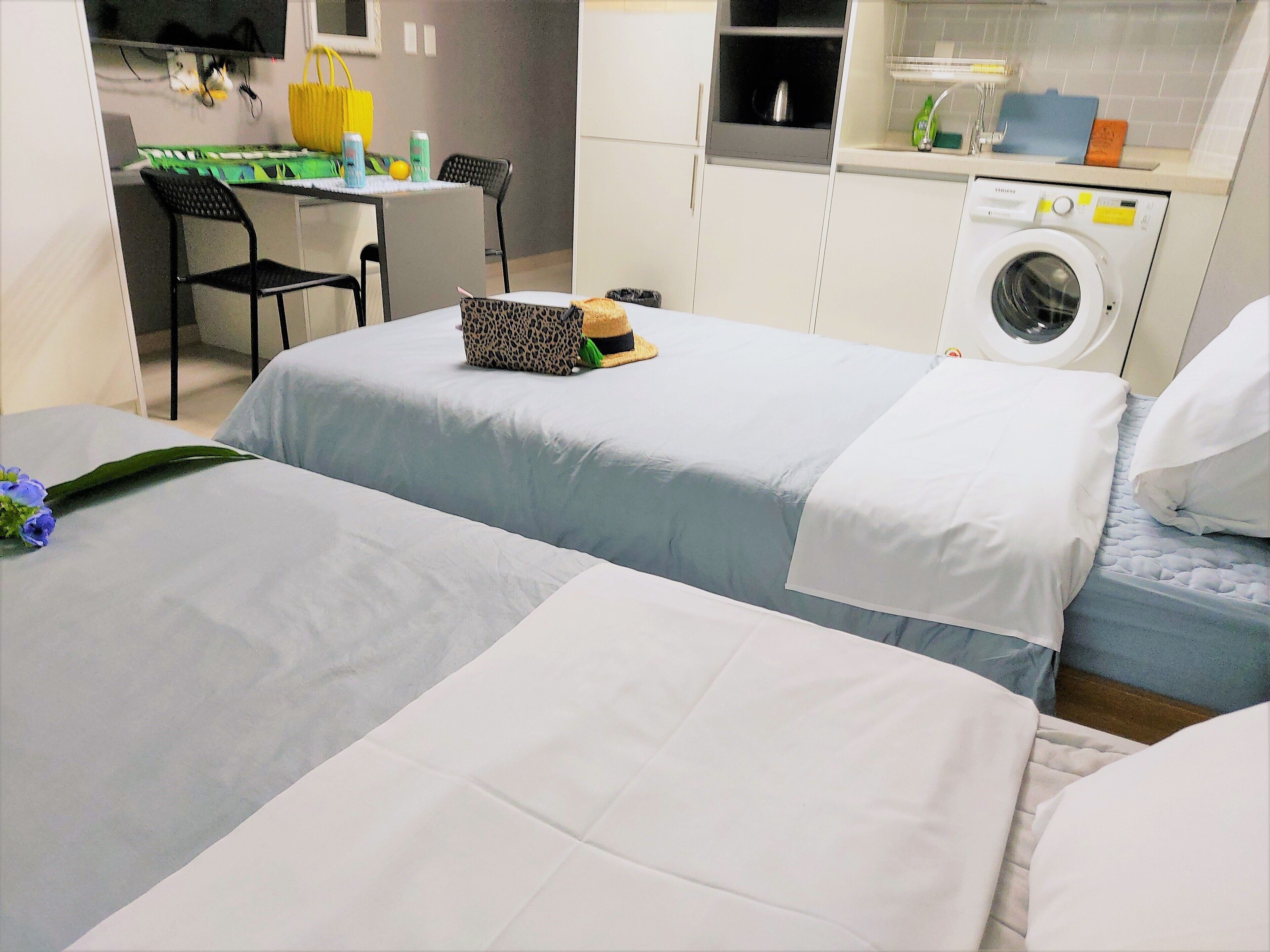 A hotel room with two beds, a desk with a chair, a washing machine, and a small kitchenette.