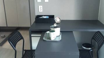 A modern, minimalist room with a dark grey table and two black chairs. A white kettle and a small clock are placed on the table.