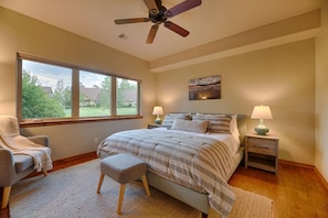 Une chambre à coucher comprenant un lit, deux tables de chevet, une chaise, une fenêtre et un ventilateur de plafond.
