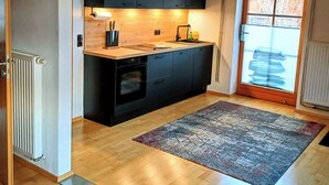 A compact kitchen with dark cabinets, a built-in oven, and a window with blinds.