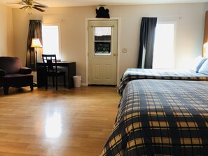 A hotel room with a bed, a chair, a desk, a ceiling fan, and a door.