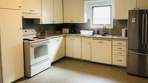 A kitchen with white cabinets, a stove, a refrigerator, and a window above the sink.