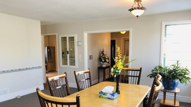 A dining room with a wooden table, six chairs, a vase with flowers, and a potted plant.