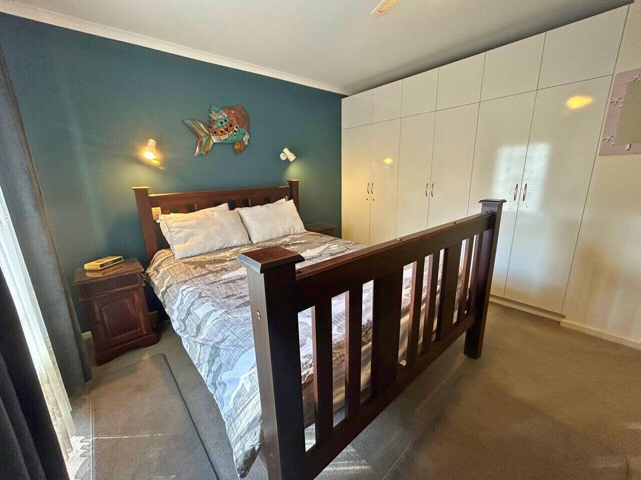 A bedroom with a bed, wooden headboard, wardrobe, nightstand, and wall decor.
