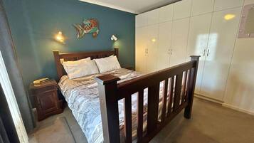 A bedroom with a bed, wooden headboard, wardrobe, nightstand, and wall decor.