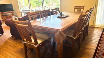 A dining area with a wooden table and chairs, a television, and a view of greenery outside.