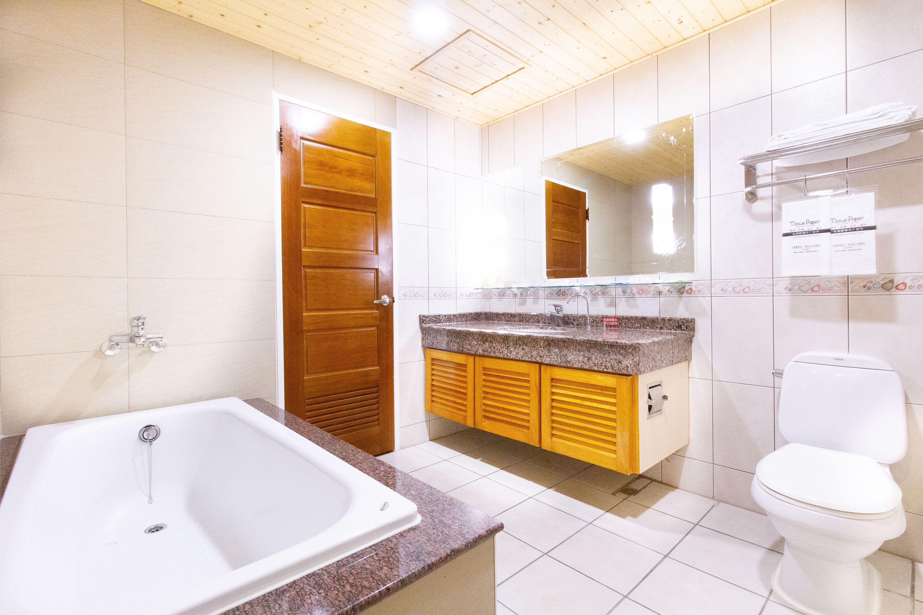 Un baño con bañera, inodoro, armarios de madera y suelo de baldosas.