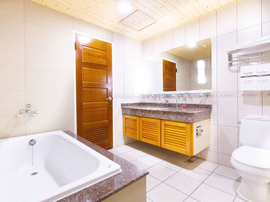 Un baño con bañera, inodoro, armarios de madera y suelo de baldosas.