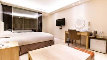 A modern hotel room with a bed, desk, chair, and a small refrigerator.