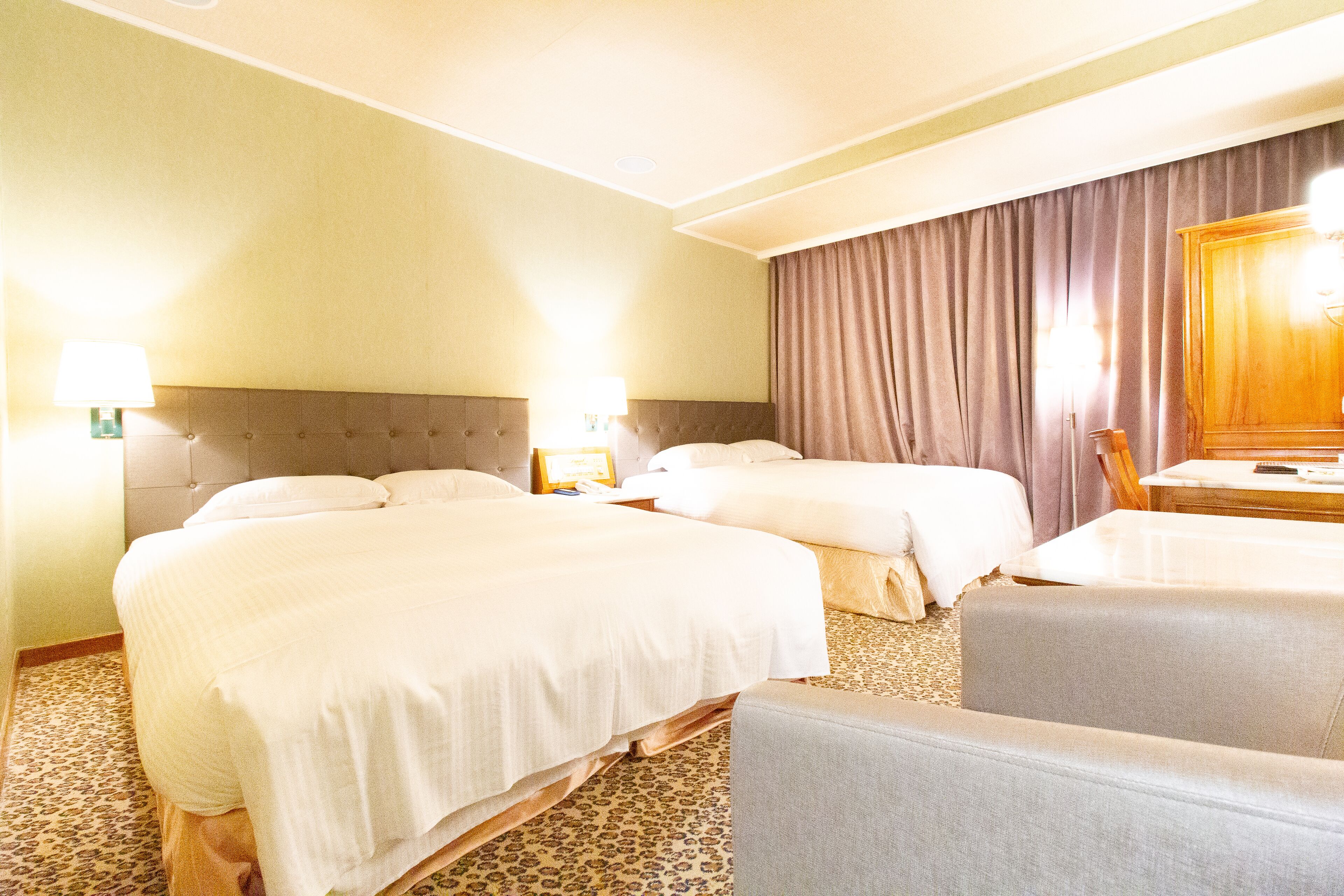 A hotel room with two beds, a desk, a chair, and a large window with curtains.