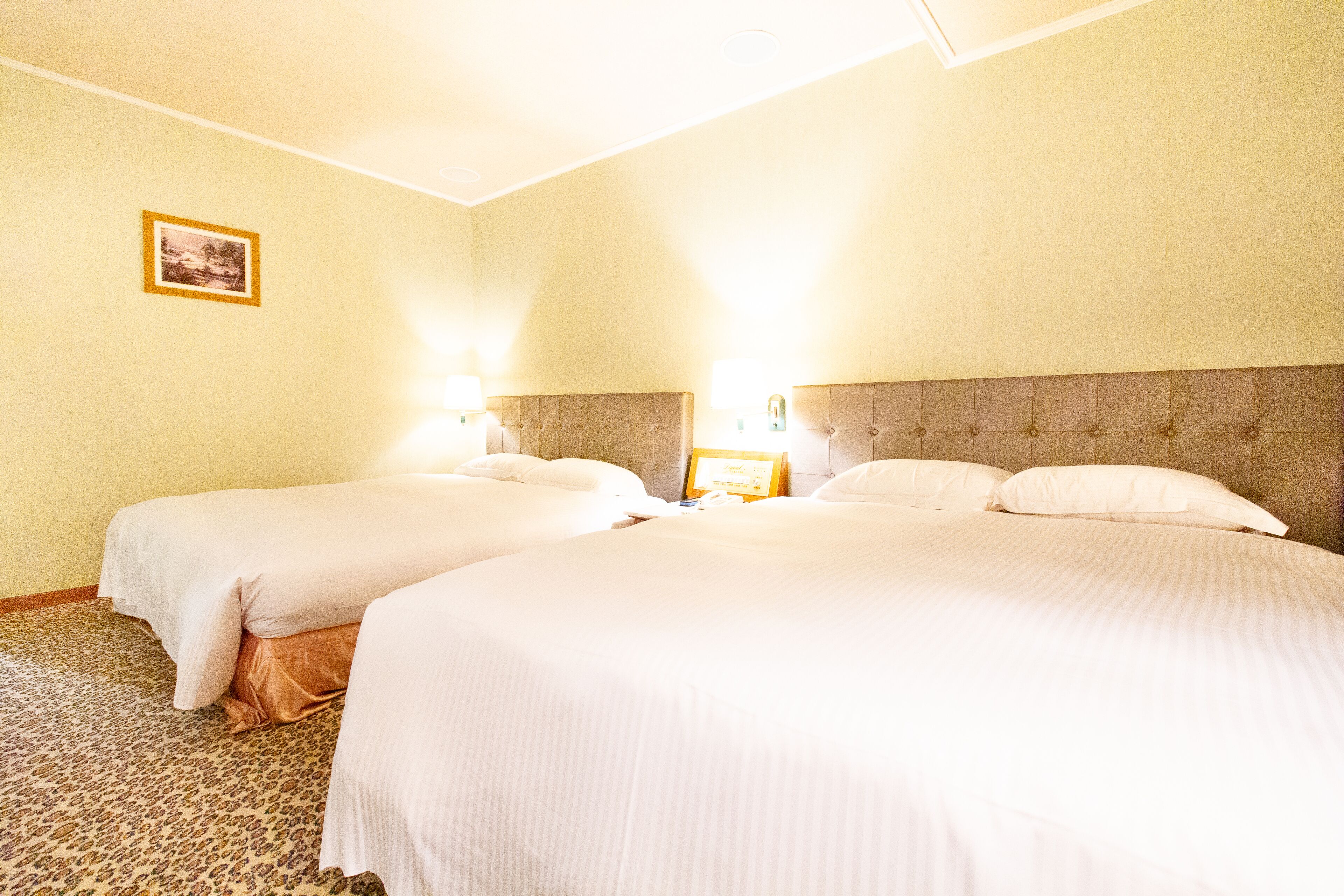 Ett hotellrum med två sängar, en sänggavel och en inramad tavla på väggen.