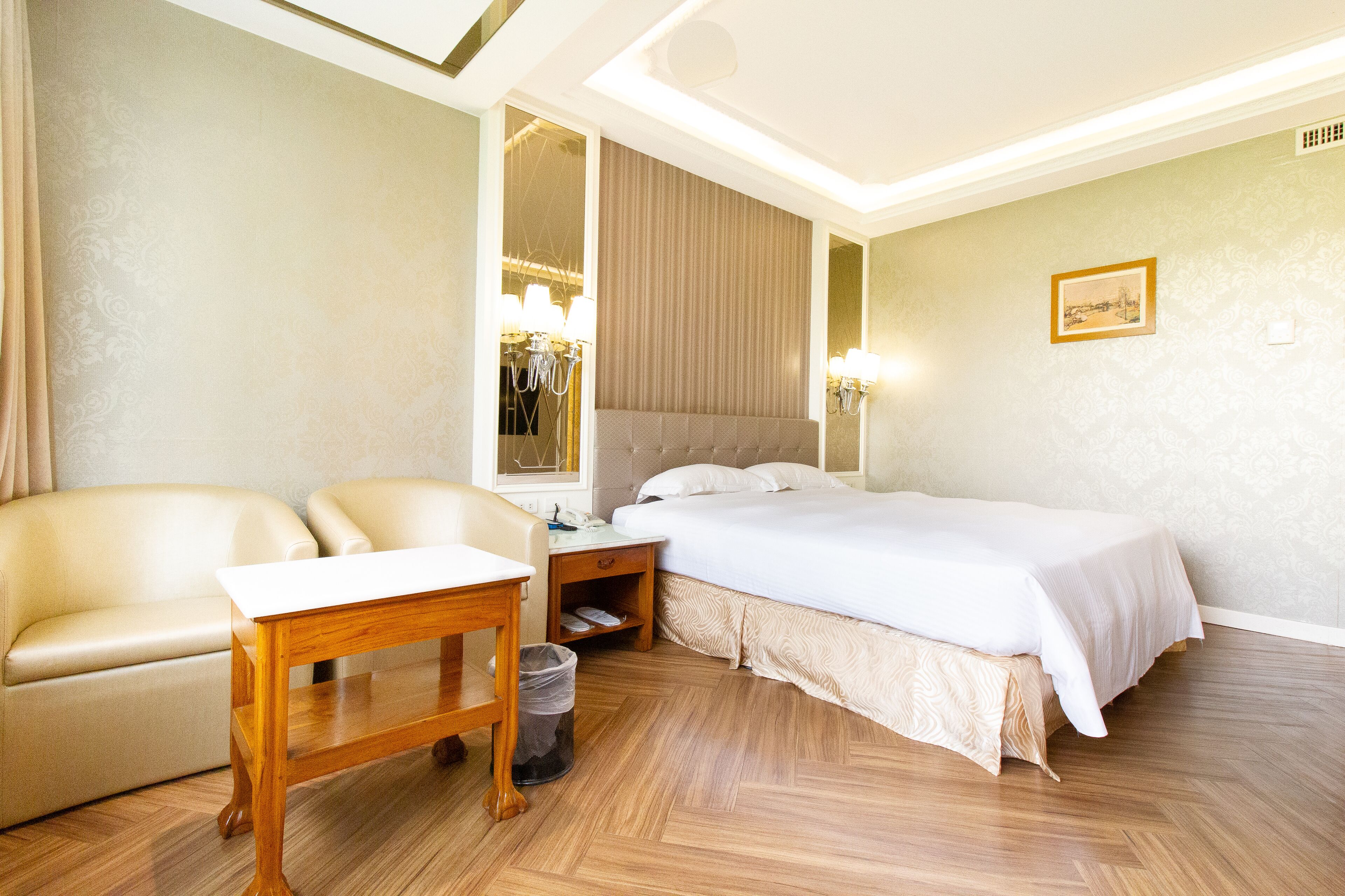 Een hotelkamer met een bed, twee stoelen, een houten tafel, een nachtkastje en een spiegel.