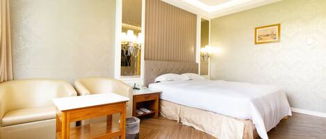 Een hotelkamer met een bed, twee stoelen, een houten tafel, een nachtkastje en een spiegel.