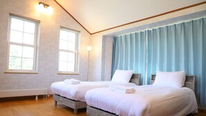 Un dormitorio con dos camas, suelo de madera y ventanas grandes con cortinas.
