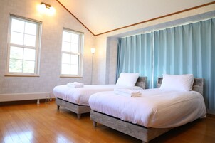 Une chambre avec deux lits, un plancher en bois et de grandes fenêtres avec des rideaux.