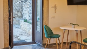A hotel room with a bed, a small table with chairs, a TV mounted on the wall, and a door leading to an outdoor area.