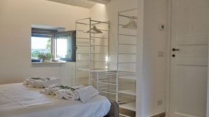A bedroom with a bed, a window, a drying rack, and a door.
