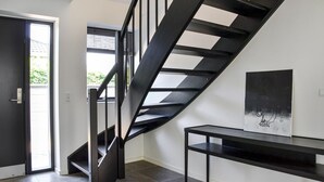 Un interno moderno con una scala a chiocciola nera, una porta che dà sull'esterno e un tavolo nero minimalista con un'opera d'arte astratta.