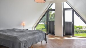 Camera da letto con un letto grande, una lampada da comodino e vista su un paesaggio verde attraverso una grande finestra.
