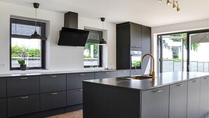 Cucina moderna con mobili scuri, isola centrale, cappa aspirante nera, luci a sospensione e vista sul verde.