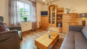 Un salon comprenant un canapé, une table basse en bois, un téléviseur et un meuble avec des portes en verre.