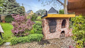Un four extérieur en pierre, doté d’une cheminée, entouré d’un jardin agrémenté d’arbustes en fleurs et d’un sentier pavé.