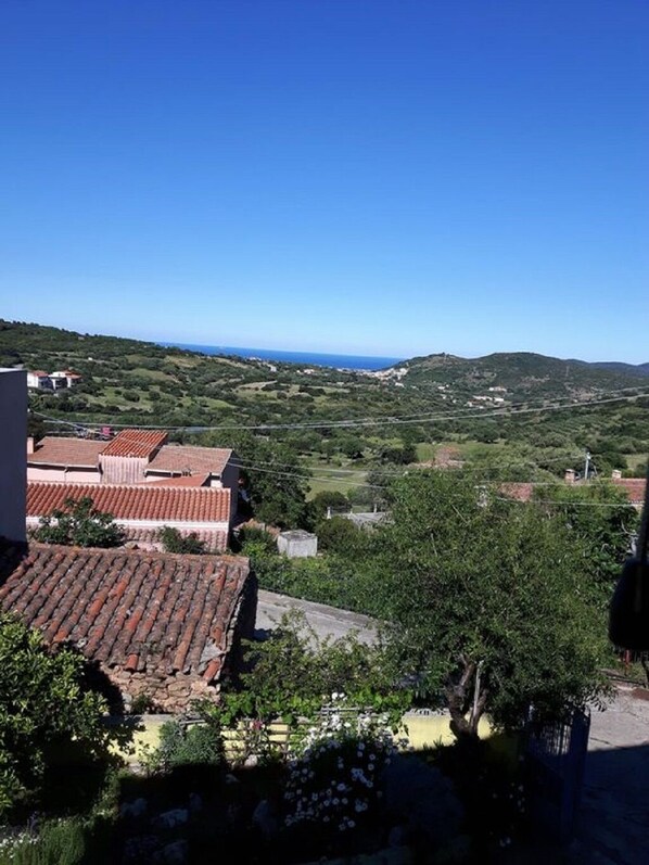 A residential area with terracotta-roofed buildings, lush greenery, and a distant view of the sea.