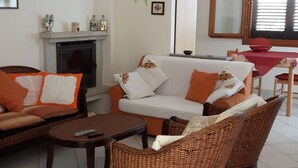 Una sala de estar con chimenea, un sofá, dos sillones de mimbre, una mesa de centro y una mesa de comedor con sillas.