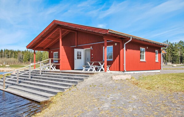 A red wooden cabin with a white door, a small porch, and a wooden staircase leading to a dock over water. - 1 bedroom stunning apartment in Kosta (Kosta)