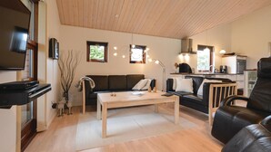 Ein modernes Wohnzimmer mit Holzboden, einem schwarzen Ledersofa, einem Couchtisch aus Holz und einem Fernseher.