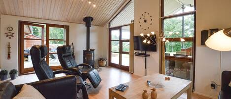 A spacious living room with a large fireplace, leather chairs, a wooden coffee table, and large windows offering a view of the outdoors.