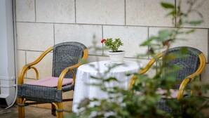 A wicker chair with a cushion, a small round table with a white tablecloth, and a potted plant with a red flower. - Apartment Matic (Dubrovnik)