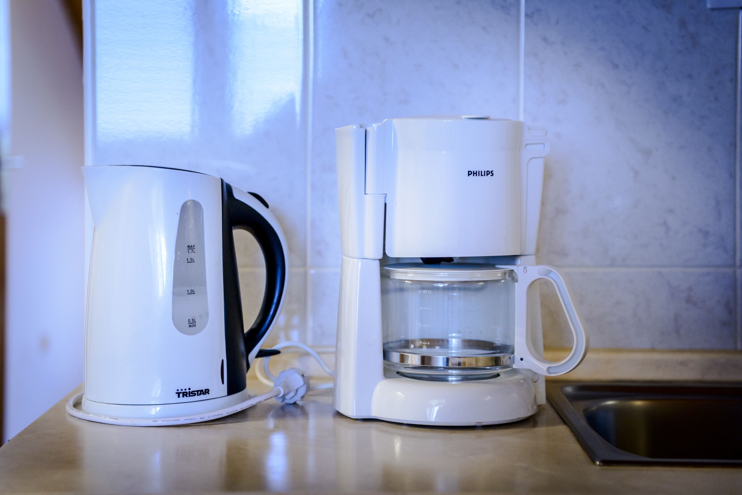 A white electric kettle and coffee maker on a kitchen counter.