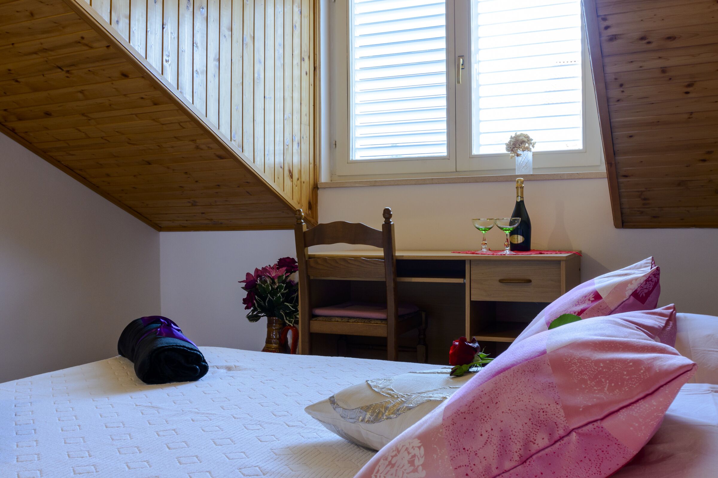 A bedroom with a bunk bed, a desk, a chair, a bottle of wine, and a vase with flowers.