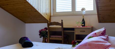 A bedroom with a bunk bed, a desk, a chair, a bottle of wine, and a vase with flowers.