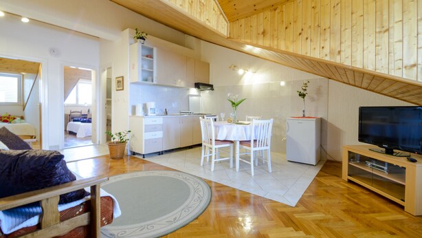 A spacious living area with a wooden ceiling, a dining table with chairs, a small kitchen, and a television on a wooden stand. - Apartment Matic (Dubrovnik)