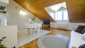 A cozy, well-lit room with a wooden ceiling, a dining area with a table and chairs, a television on a stand, and a sofa with cushions. - Apartment Matic (Dubrovnik)
