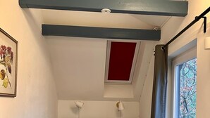 Um quarto pequeno com cama, janela com vista, parede de destaque vermelha e claraboia.