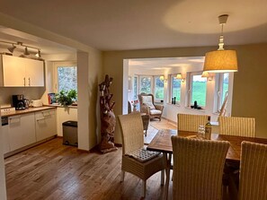 A spacious kitchen with wooden flooring, a dining area with wicker chairs, and a large window offering a view of the outdoors. - Wohnung Lotte Petersen - Willi Ohler Haus (Worpswede)