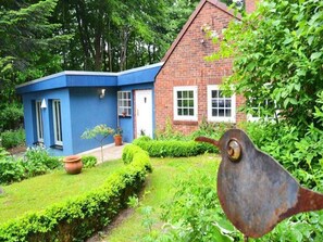 A blue building with a brick house in the background, surrounded by greenery. - Wohnung Lotte Petersen - Willi Ohler Haus (Worpswede)