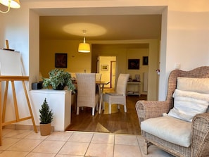 Una sala de estar acogedora con un sillón de mimbre, una mesita con una planta en maceta y un cuadro en la pared.
