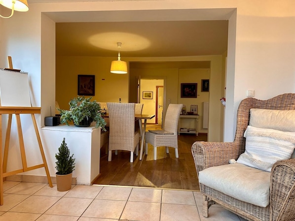 A cozy living room with a wicker armchair, a small table with a potted plant, and a painting on the wall.